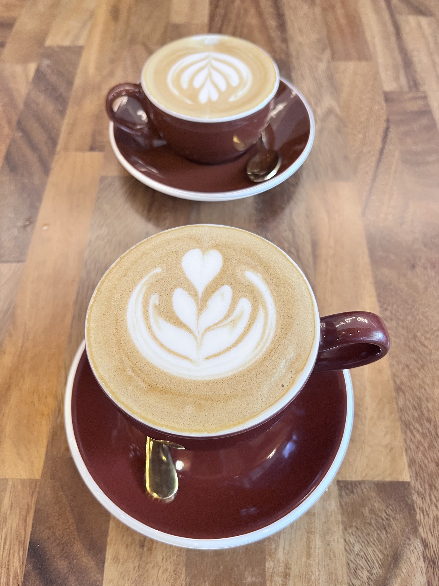 Two burgundy cups of coffee with latte art on a wood table
